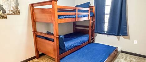 A bunk bed with blue bedding in a room with a wooden floor, an air conditioning unit, and a window with blue curtains.