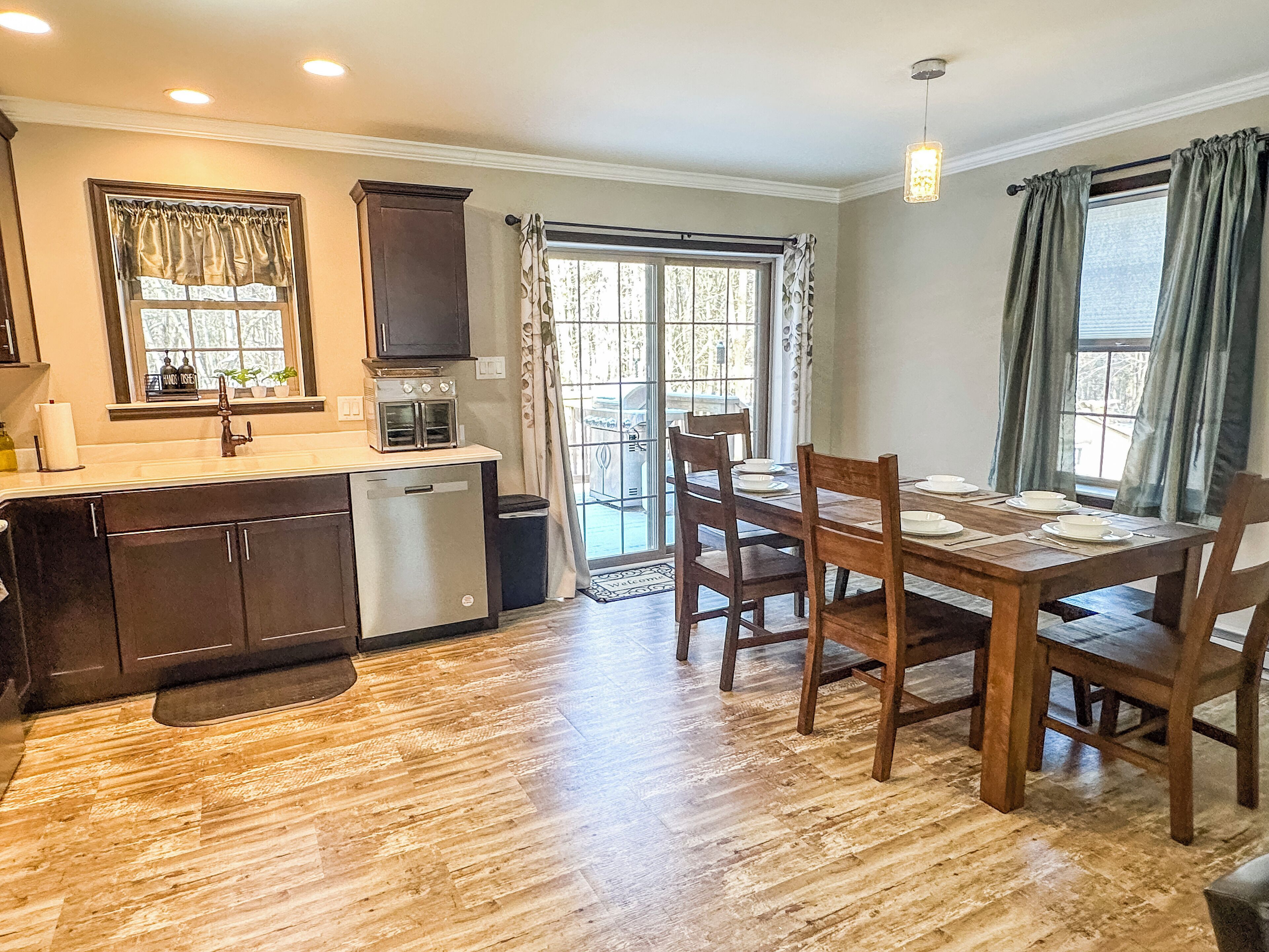 A compact kitchen with a refrigerator, microwave, and oven. There is a dining table with chairs and a window with curtains.