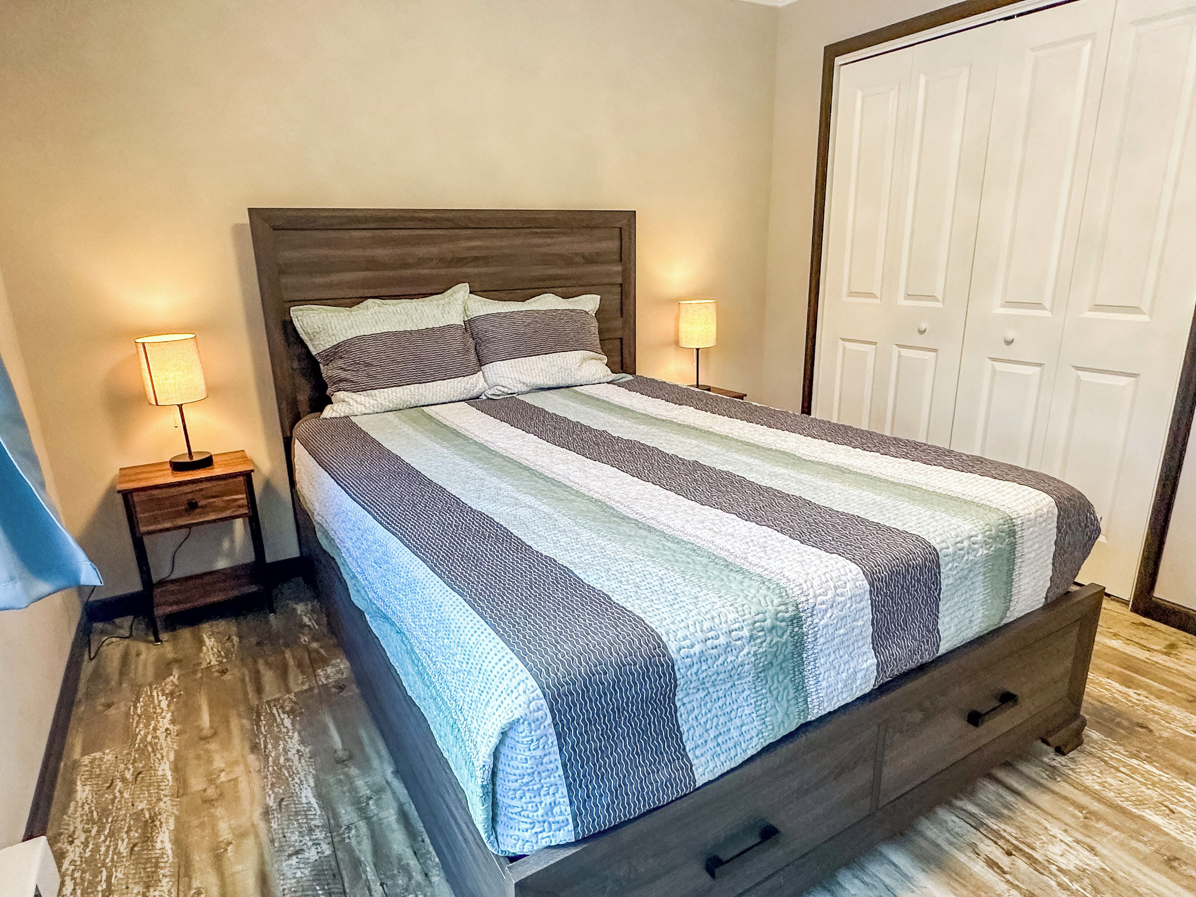 A bedroom with a bed, two bedside tables, a nightstand, a wooden headboard, and a wardrobe.
