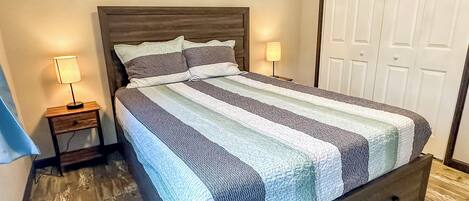 A bedroom with a bed, two bedside tables, a nightstand, a wooden headboard, and a wardrobe.
