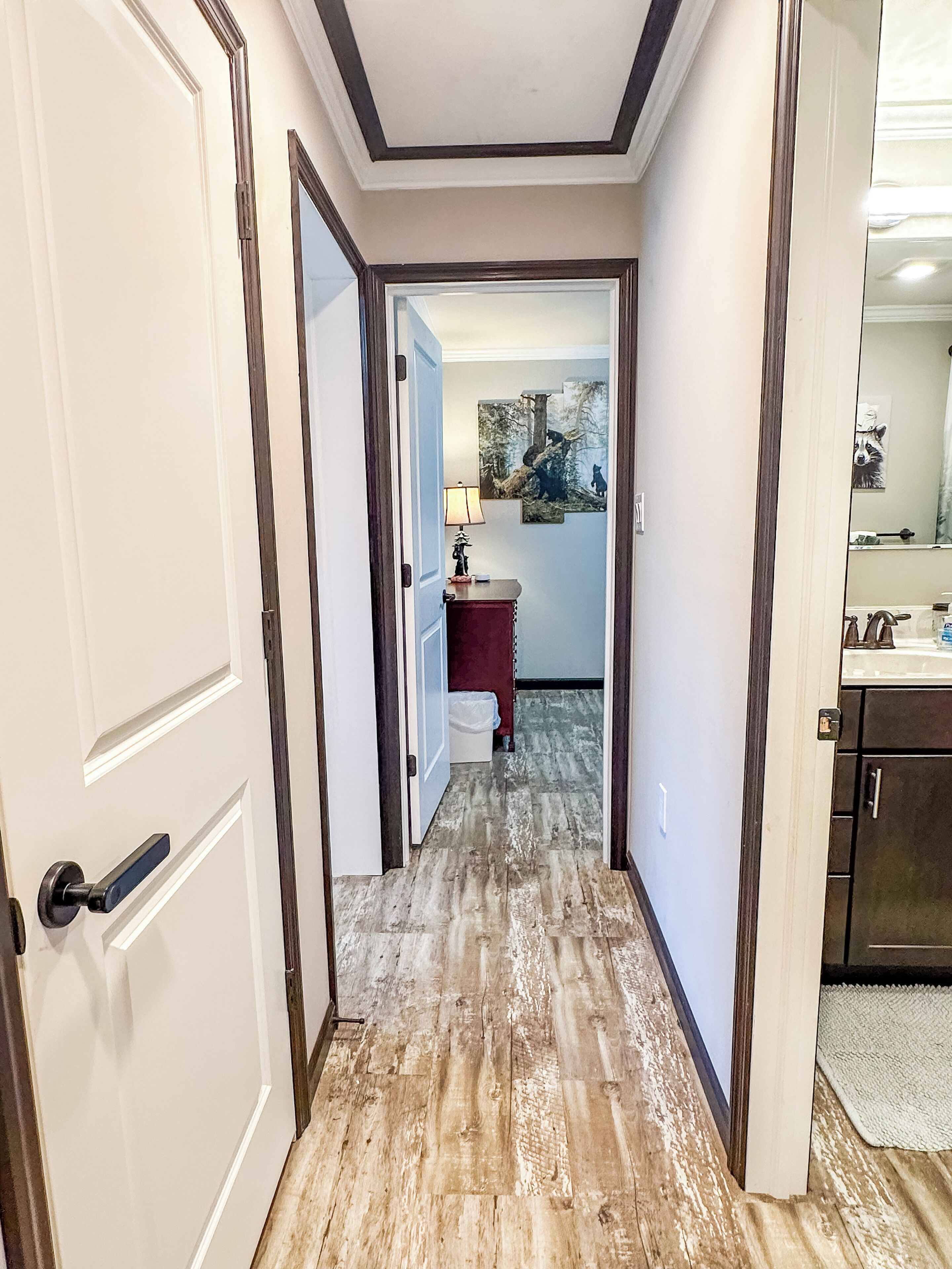 A hallway with wooden flooring leading to a bathroom with a sink and mirror.