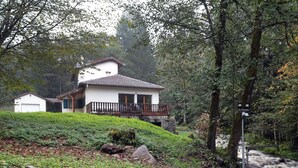 Een wit huis met een balkon, omringd door weelderige begroeiing en een stromende rivier.