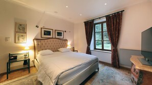 Een keurig opgeruimde slaapkamer met een groot bed, nachtlampjes, een televisie en een raam met gordijnen.