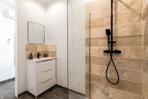 A modern bathroom with a glass-enclosed shower, a white vanity with a mirror, and beige tiles.
