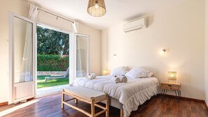 A bedroom with a bed, bench, bedside table, and an open sliding door to a garden. - Sòle - Peri -  Maison climatisée avec piscine (Peri)