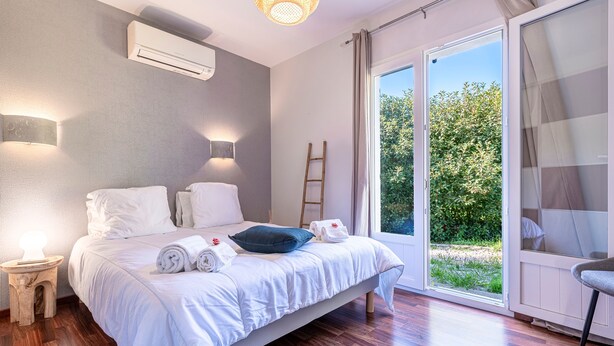 A bedroom with a bed, two bedside tables, a nightstand, a ladder, and a view of greenery through a sliding glass door. - Sòle - Peri -  Maison climatisée avec piscine (Peri)