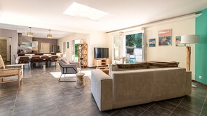 A modern living room with a sofa, dining table, and chairs, a kitchen area, and a TV. - Sòle - Peri -  Maison climatisée avec piscine (Peri)