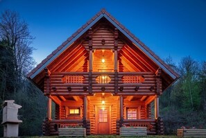 A log cabin with a central door, two windows on each side, and a porch with railings.