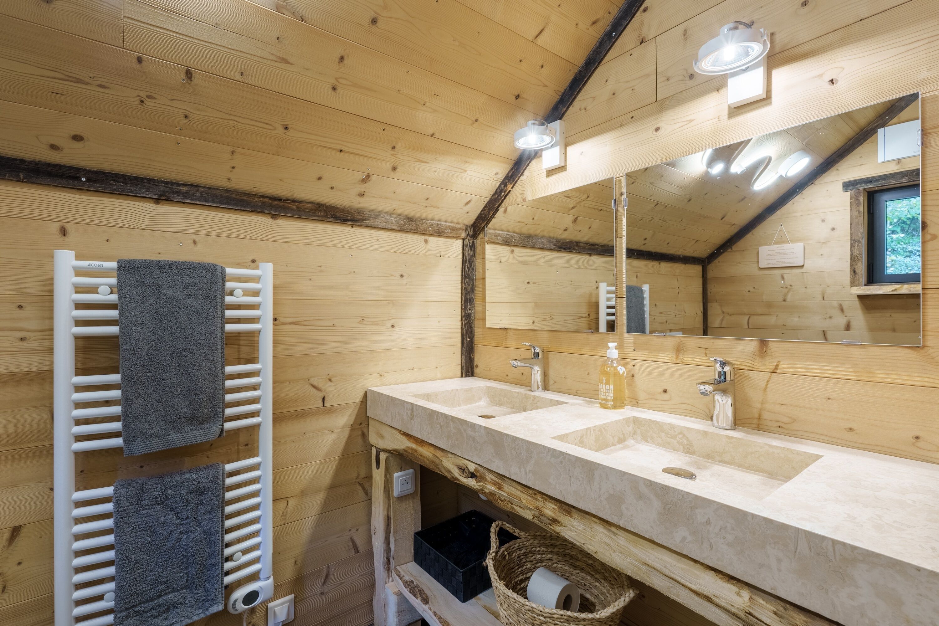 A wooden cabin bathroom with a double sink, towel rack, and a mirror.