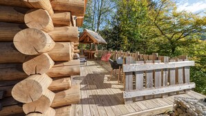A wooden log cabin with a deck, surrounded by trees.