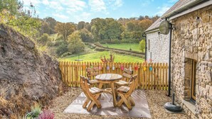 A patio with a wooden table and chairs, surrounded by a stone wall and a wooden fence.