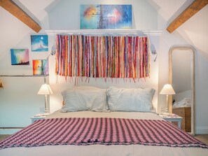 Ein Schlafzimmer mit einem Bett, zwei Nachttischen, einem Spiegel und Wandbildern.