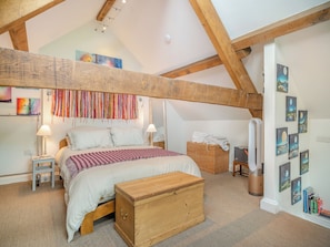 A bedroom with a bed, bedside tables, a wooden chest, a hanging tapestry, and wall art.