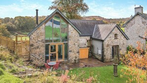 A stone house with a glass conservatory, a wooden door, and a small patio with chairs.