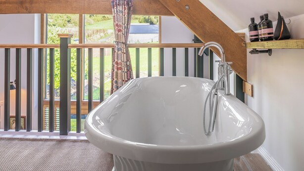 A bathroom with a freestanding bathtub, a wooden ceiling, and a view of a garden through large windows.