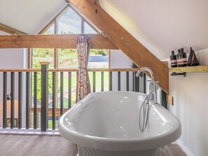 Ein Badezimmer mit einer freistehenden Badewanne, Holzboden und Blick auf einen Garten durch große Fenster.