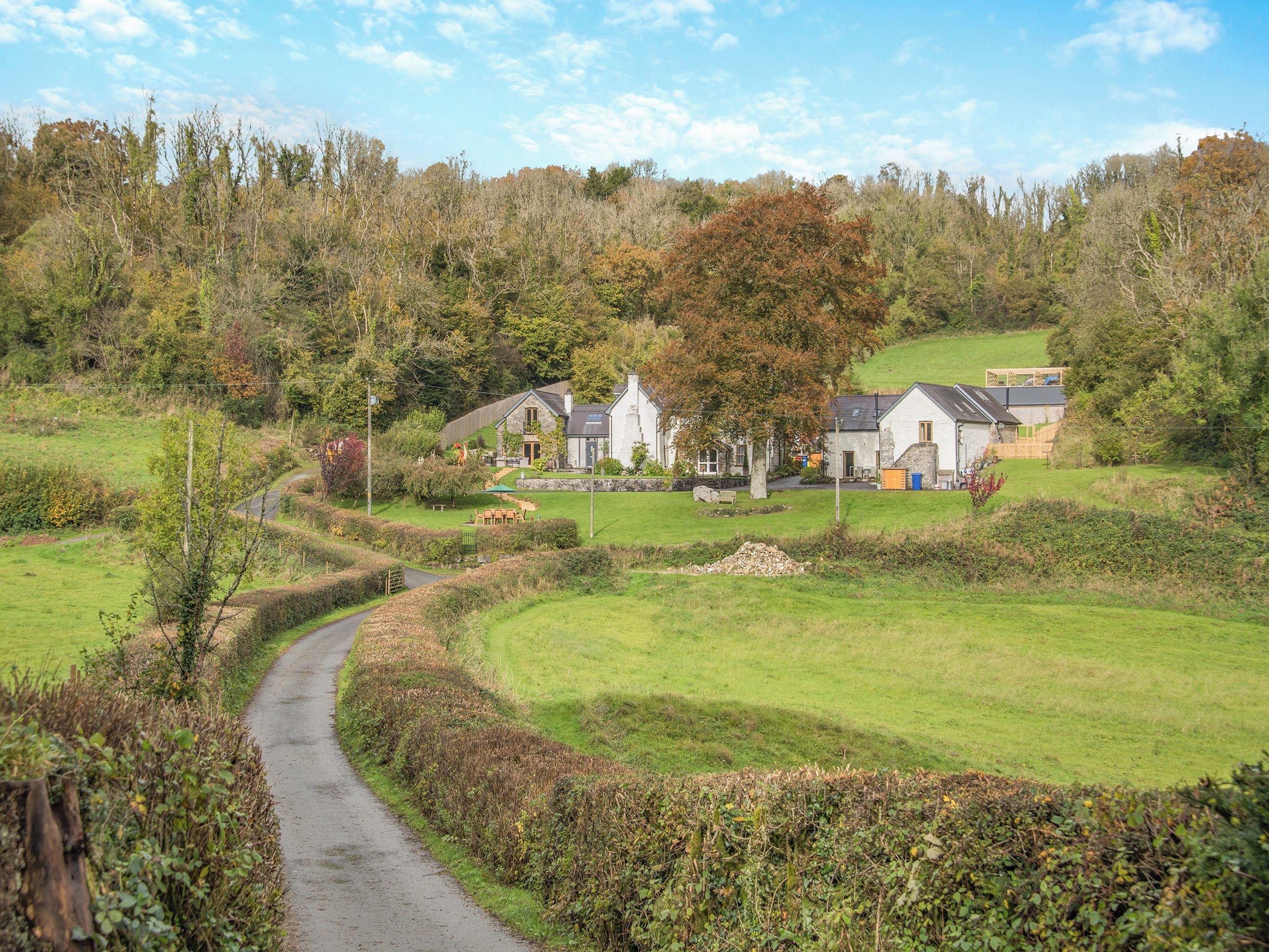 A rural setting with a pathway leading to a cluster of stone houses surrounded by greenery and trees.