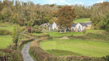 A rural setting with a pathway leading to a cluster of stone houses surrounded by greenery and trees.