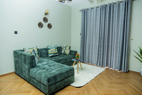 A living room with a green sectional sofa, a small round table with a plant, and a white rug.