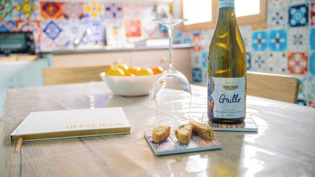 A table with a bottle of Grillo wine, a glass, a notebook, and some food items.