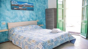 A bed with a patterned bedspread, a nightstand, a tall cabinet, and a door leading outside.