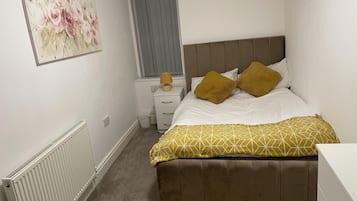 Un dormitori amb un llit, una taula de nit, una làmpada, un radiador i un quadre a la paret.