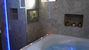 Ett spa-rum med en vägg av marmor, ett stort badkar och en hylla med krukväxter.