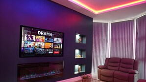 Ett modernt vardagsrum med en stor tv-skärm som visar ett dramakanal, en bekväm fåtölj och en dekorativ hylla med små föremål.