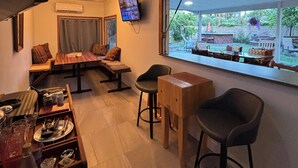 A cozy restaurant interior with a long dining table, bar stools, a sofa, and a TV mounted on the wall. - Beautifully restored charming MCM home in the heart of Tempe.  (Tempe)