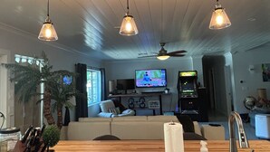 A modern living room with a wooden floor, a large TV, and three pendant lights. - Beautifully restored charming MCM home in the heart of Tempe.  (Tempe)