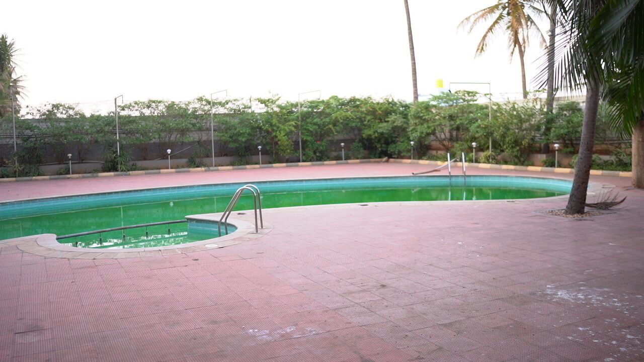 Piscina con scaletta in metallo, circondata da una terrazza in piastrelle rosse e vegetazione.