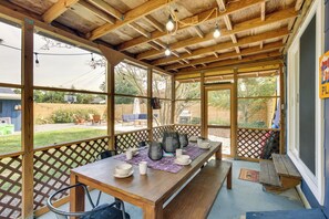 Een overdekt terras met een houten eettafel, omringd door een houten hek en grote ramen.