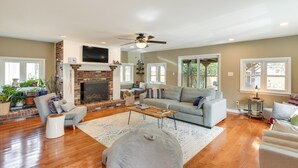A spacious living room with hardwood flooring, a fireplace, a ceiling fan, and a large window providing natural light. - The Blue House. 
A Family Beach House or Winter Getaway in Cape May (Cape May)