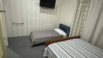 Een kleine, compacte kamer met een eenpersoonsbed, een nachtkastje, een aan de muur bevestigde televisie en een gordijn voor het raam.