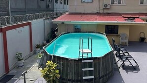 Una piscina exterior amb una escala, envoltada de plantes en testos, i al costat d'un edifici amb teulada vermella.
