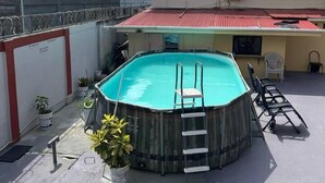 Una piscina al aire libre con una escalera, rodeada de plantas en macetas y mobiliario de exterior.