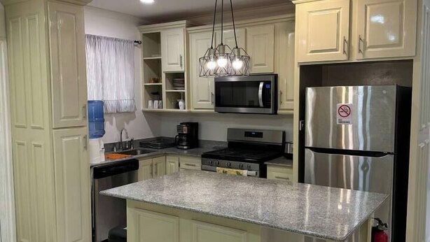 Una cocina moderna con armarios color crema, encimera de granito, electrodomésticos de acero inoxidable y una lámpara colgante.