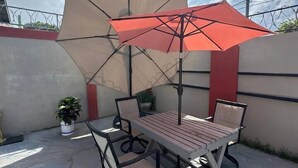 Un patio al aire libre con una mesa y sillas de madera, un paraguas color beige y una planta en maceta.