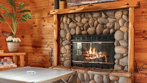 Une cheminée en pierre avec un feu de bois, des murs en bois, une table et une plante en pot.