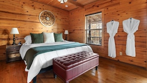 Une chambre de style cabane en bois, avec un lit, un banc capitonné, deux lampes, un élément décoratif mural et deux peignoirs accrochés au mur.