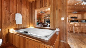 L’intérieur d’un chalet en bois, avec une grande baignoire, des meubles en bois et un coin cuisine visible à travers une porte ouverte.