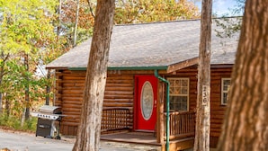 Une cabane en rondins avec une porte rouge, portant le numéro 236, et une véranda avec un banc.