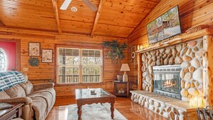 Een gezellig interieur van een blokhut met een stenen openhaard, houten wanden, een comfortabele bank en een televisie boven de openhaard.