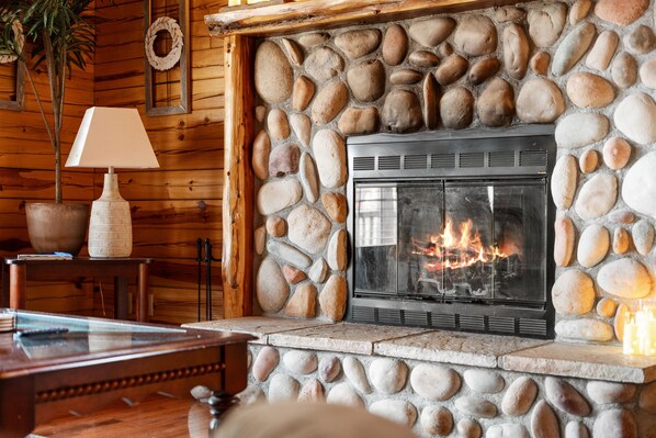 Une cheminée en pierre avec un par-feu moderne, des murs en bois et une table avec une lampe.