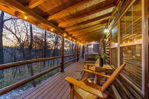 A wooden deck with a table and chairs, overlooking a forested area.