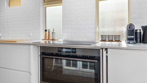 Una cocina moderna con armarios blancos, horno integrado, lavavajillas y cafetera sobre la encimera.