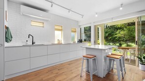 Una cocina moderna con armarios blancos, una isla central con taburetes y grandes ventanales con vistas al exterior.