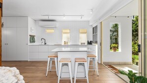 Una cocina moderna con una isla central, taburetes de bar y vista a zonas verdes a través de un ventanal.