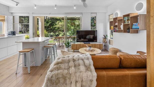 Una cocina moderna con una isla central, un comedor con una mesa redonda, una sala de estar con sofá y televisor.