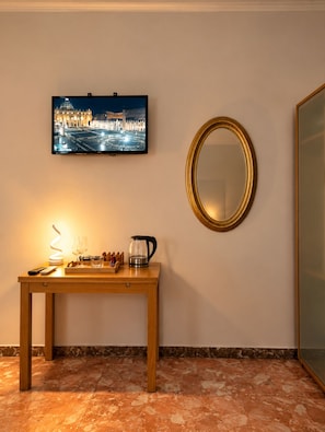 A hotel room with a television mounted on the wall, a round mirror, a wooden table with a tray, a coffee pot, and a remote control. - Colosseo Rooms (Rome)